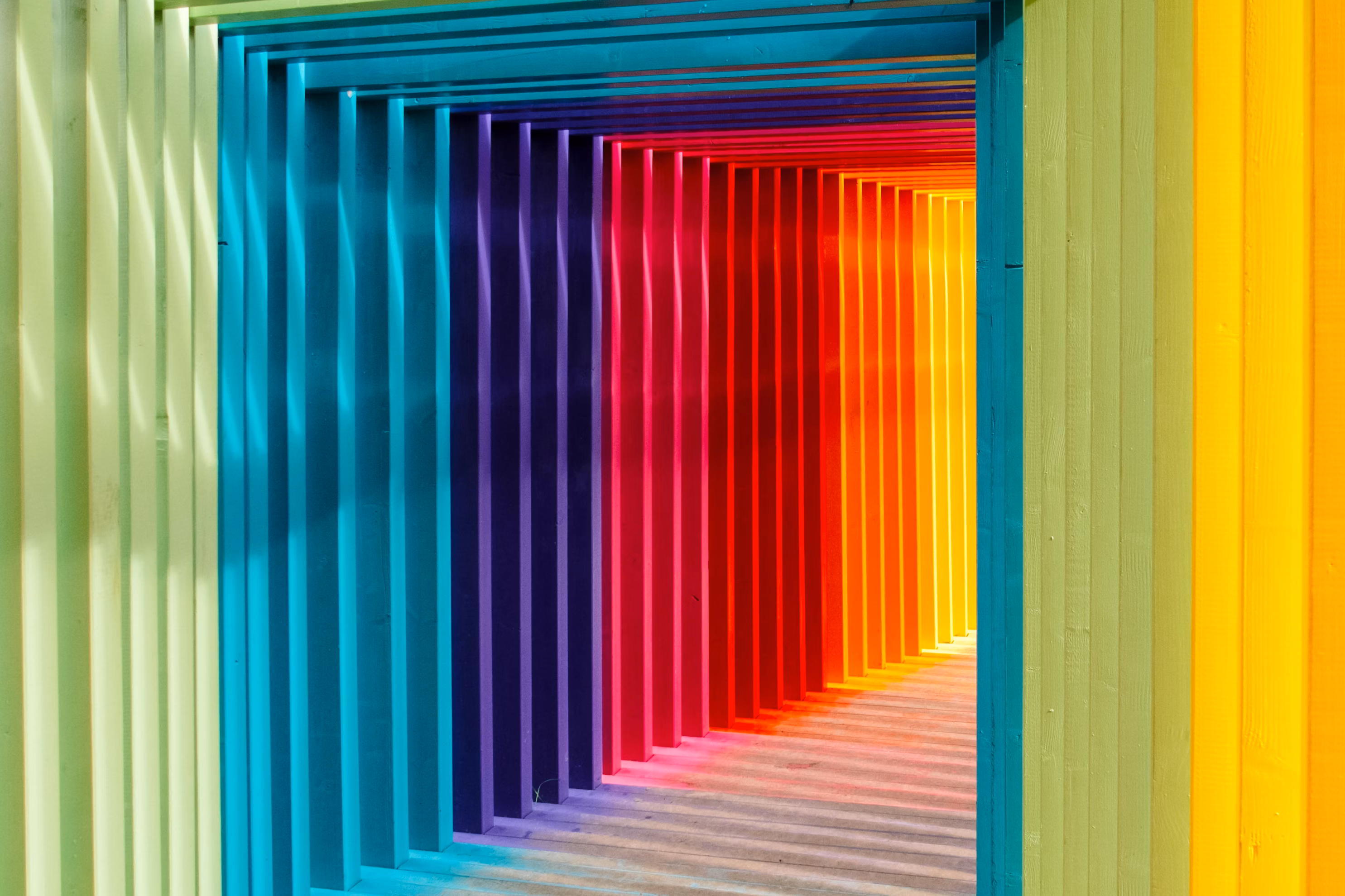 A corridor of multi-colors frames, creating a rainbow hallway, is well lit and the light is blending colors inside the corridor.