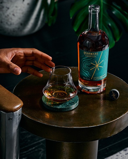 A glass of Starward on a marble coaster beside the Starward x Lagavulin bottle